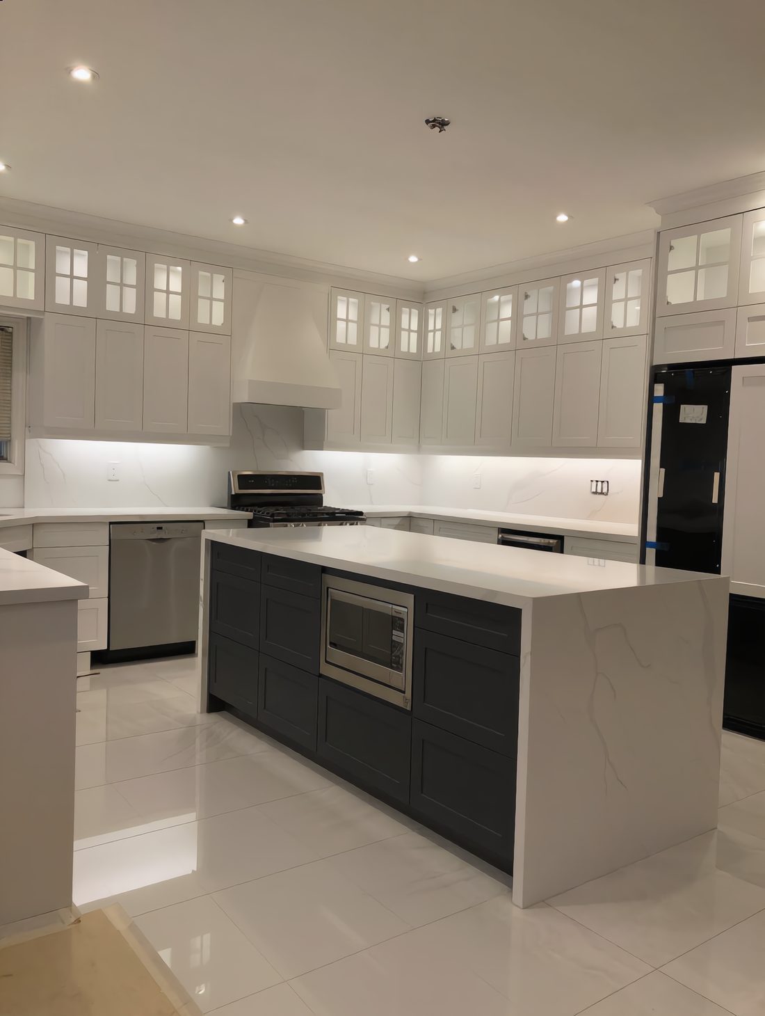 White shaker kitchen with glass-front upper cabinets and a marble-topped island over a dark panelled base with an integrated microwave