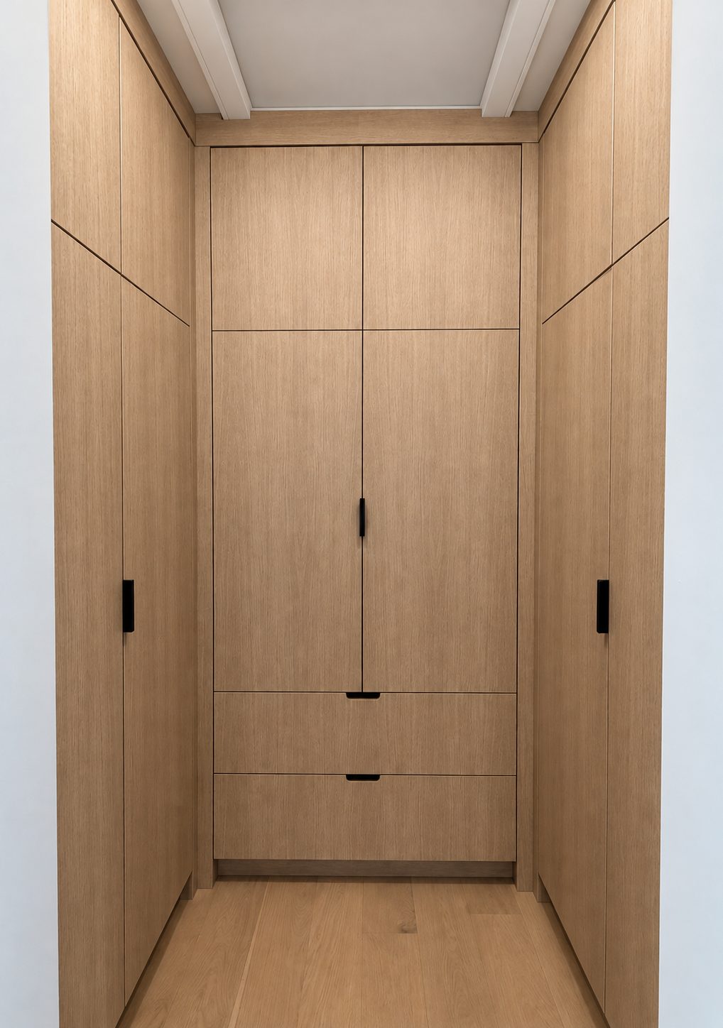 White oak dressing alcove lined floor to ceiling, with a centre wardrobe on recessed black pulls and full-height cabinets to either side
