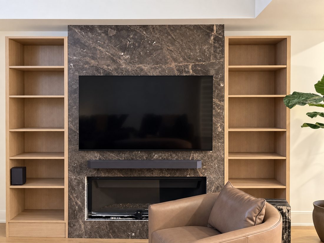 Living room media wall in dark veined marble with a mounted television, a linear fireplace below, and white oak open bookcases built in to either side