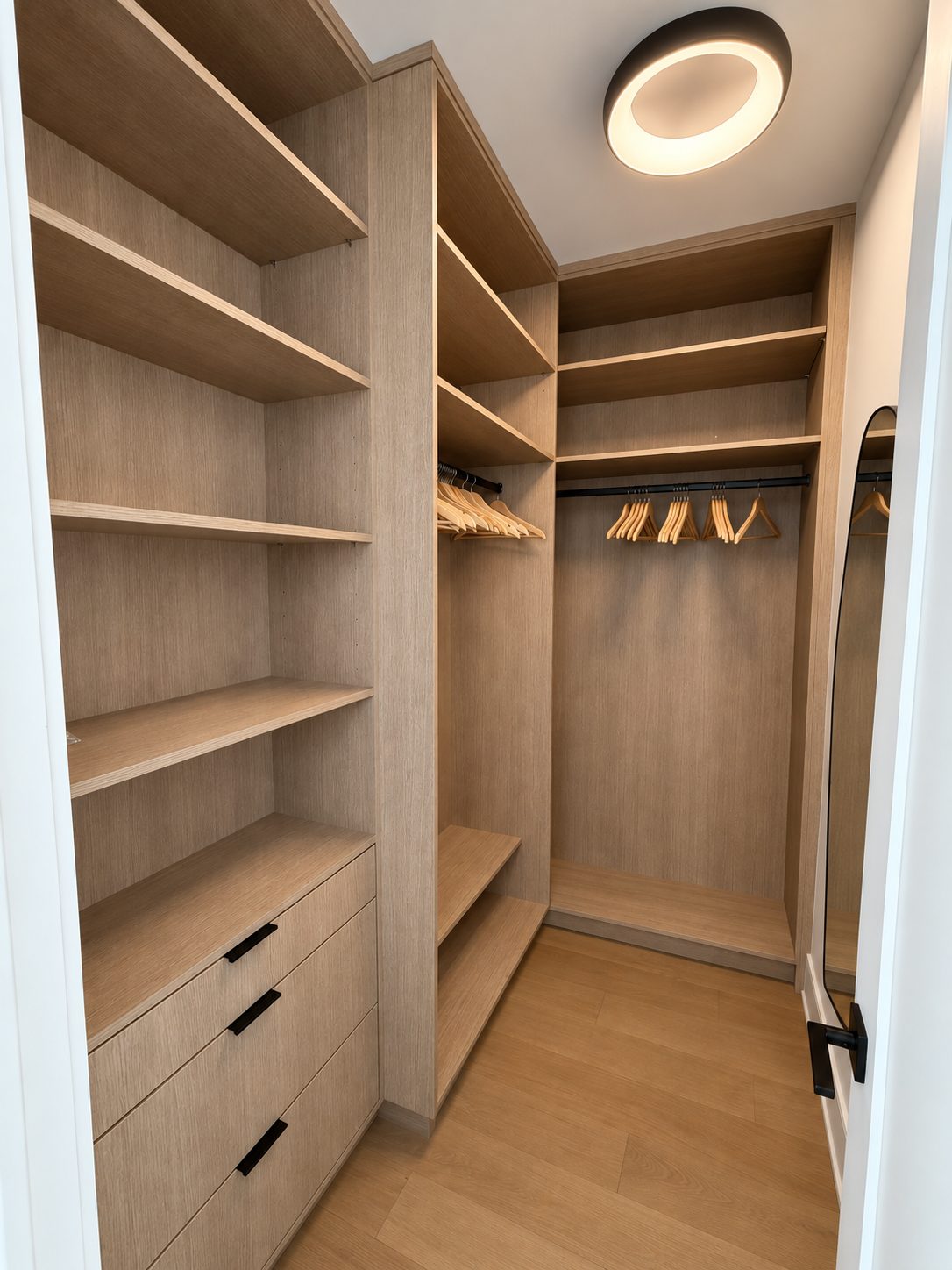 White oak walk-in closet with open shelving, two levels of hanging on wooden hangers, a drawer bank, and a full-length mirror